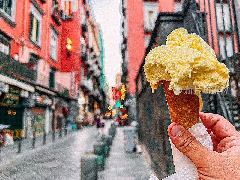 在圣加埃塔诺广场的Dei Tribunali大街上，手拿着一个充满活力的黄色柠檬味意大利冰淇淋，冰淇淋在蛋筒里融化
